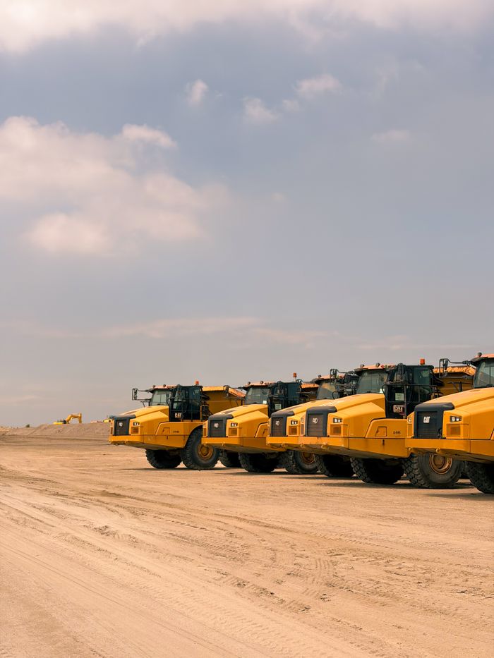 Heavy-duty dump trucks lined up on a construction site under a bright sky.